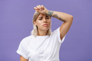 Woman in white t shirt with hand over her forehead in a distressed manner with purple background